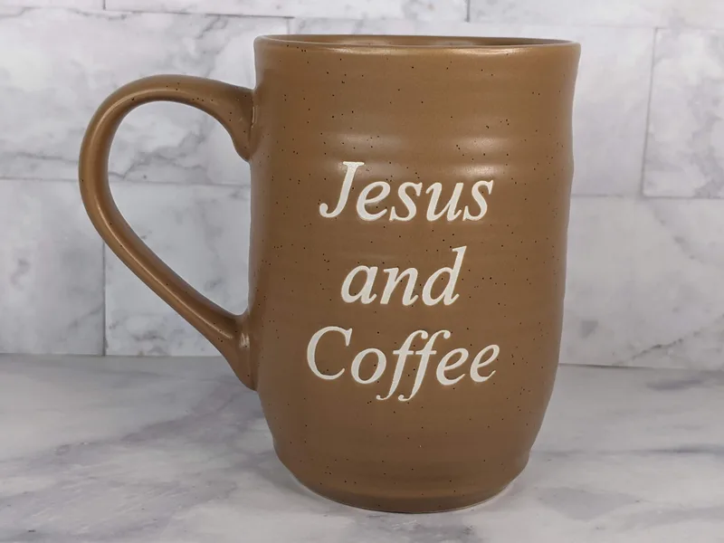 A brown Christian coffee mug with a faith-based message, "Jesus and Coffee"