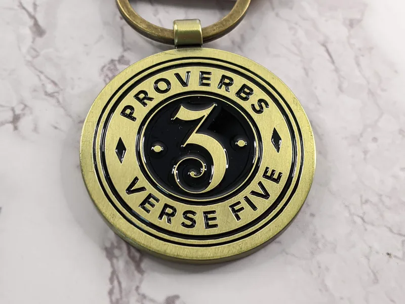A gold metal keychain with a Bible verse from Proverbs 3:5 which says, "Trust in the Lord."