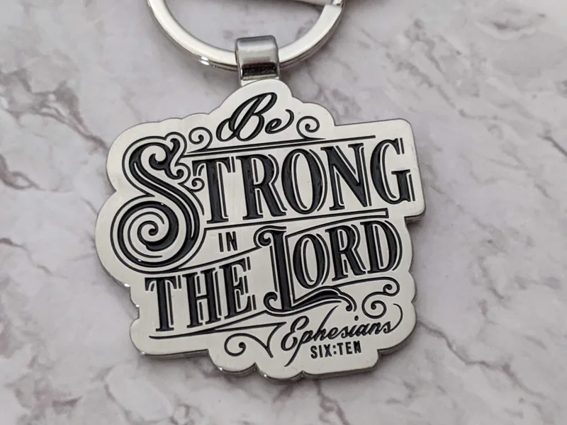A metal scripture keyring with the Bible verse Ephesians 6:10: Be strong in the Lord and in His mighty power.