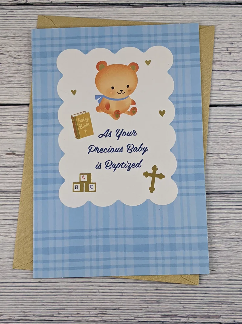 A baby baptism greeting card with a blue plaid cover that features images of a teddy bear, Bible, toy blocks, and a cross.