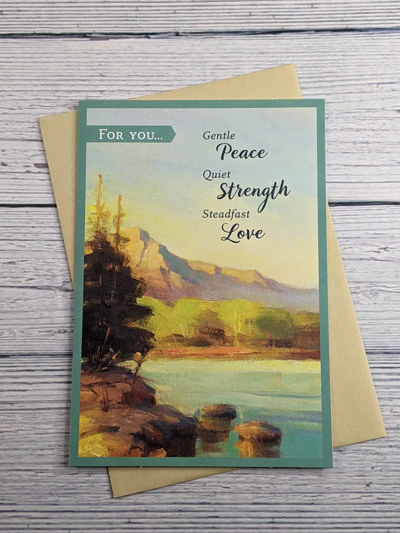 A religious encouragement card with an image of a mountainside lake surrounded by trees.