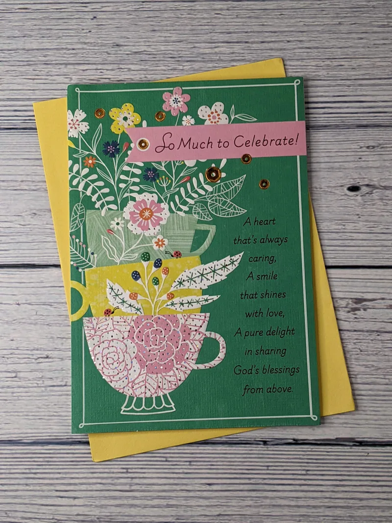 A birthday greeting card for a woman with a green cover, an image of stacked teacups with flowers in them, and a Christian sentiment.