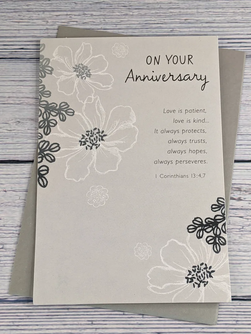A gray and silver religious anniversary card by American Greetings with an image of flowers and a Bible verse sentiment about love.