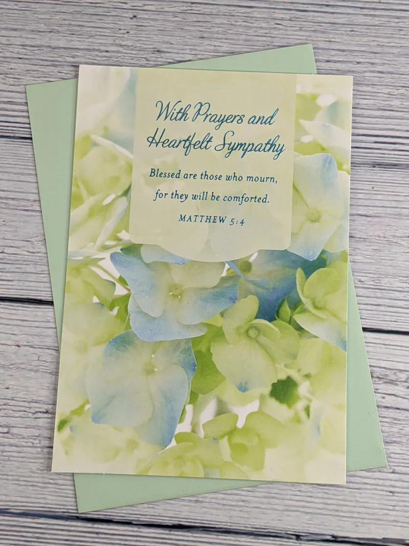 A sympathy card with a religious message and Bible verse. The cover has an image of blue and green flowers.