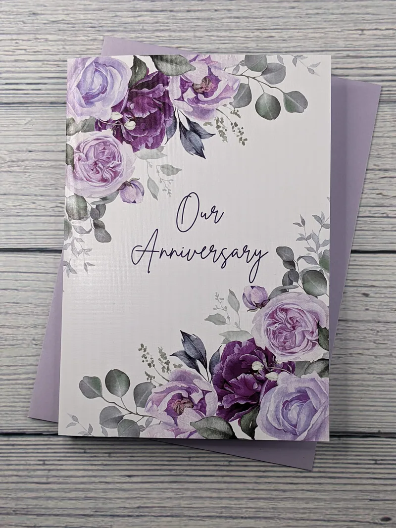 A textured greeting card that has a white background with purple flowers at the corners and the words "Our Anniversary" in the middle.