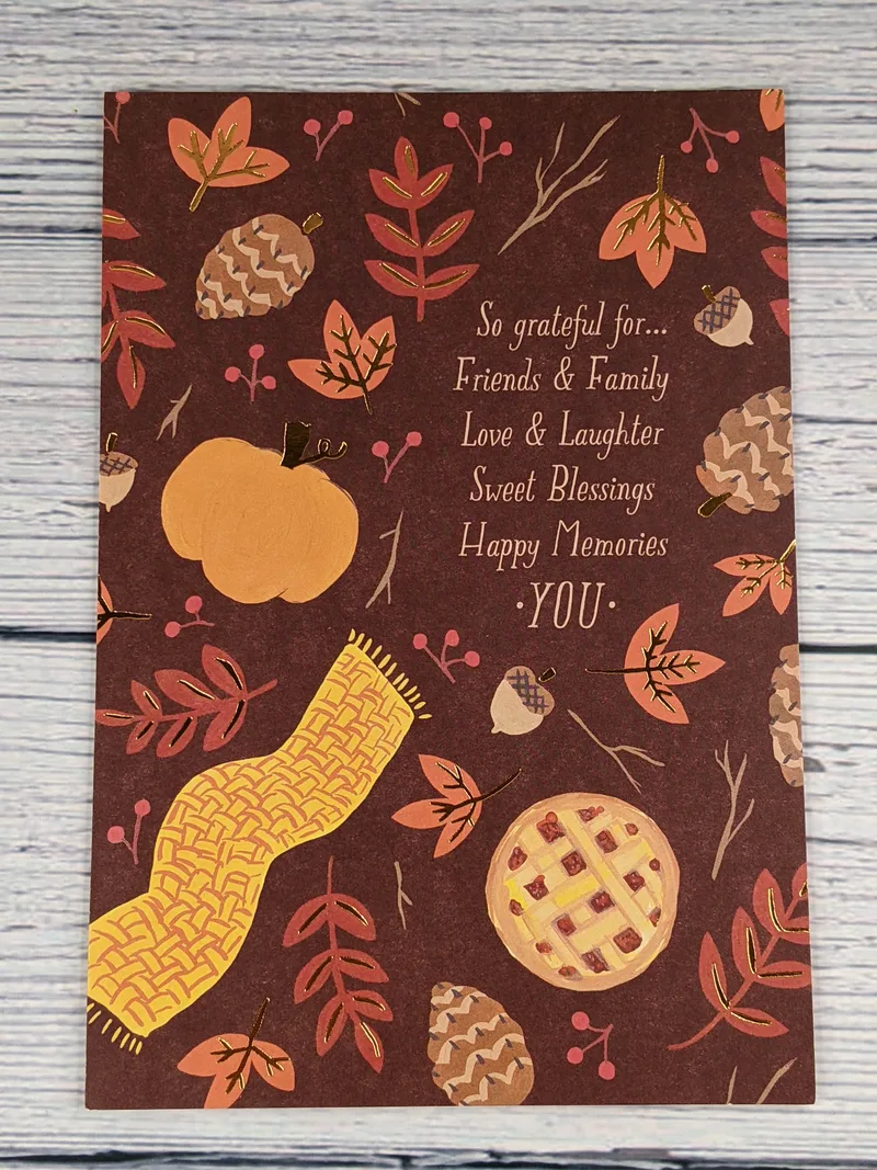 A Thanksgiving card with a brown background and images of orange leaves, brown pinecones, a yellow scarf, an orange pumpkin and a statement of gratitude.
