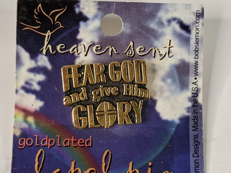 A gold metal lapel pin with a cross design and the words, "Fear God and give him glory."