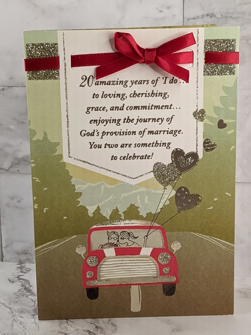 A 20th anniversary greeting card with a red satin bow, religious sentiment, and an image of a red car traveling on a road. 