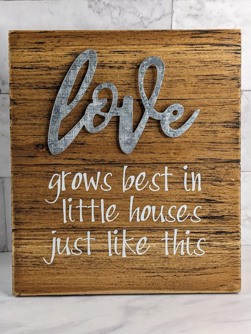 A rustic wooden plaque that has an inspirational message, "Love grows best in little houses just like this."