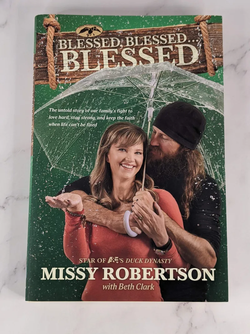 A hardcover book with a dustjacket featuring a couple under an umbrella. The book title is Blessed, Blessed, Blessed by Missy Robertson.