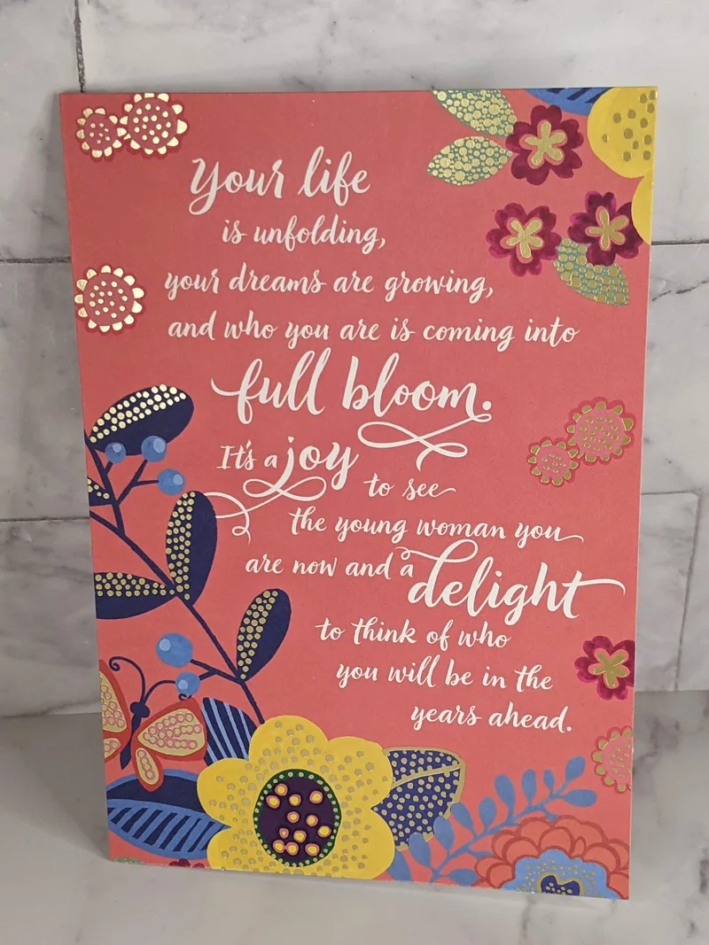 A religious graduation card for a young woman, with a coral cover that has a yellow and blue flower design.