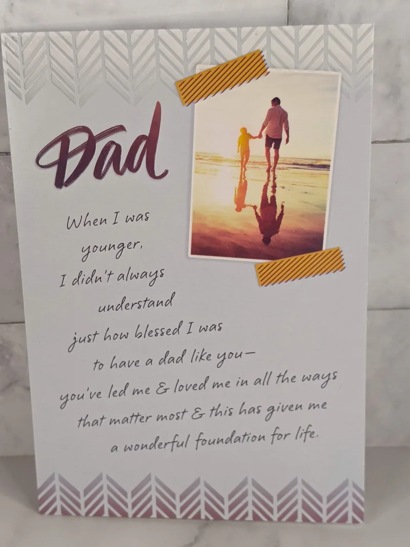 A religious Father's Day greeting card with an image of a dad holding his young daughter's hand on the beach at sunset.