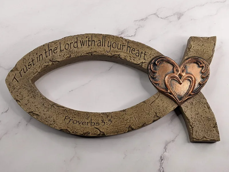 A resin Ichthus wall decor shaped like a fish symbol, features a Trust in the Lord Bible verse and a design of copper toned hearts.