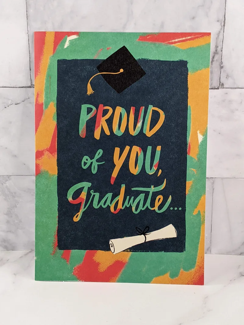 A religious graduation card with a green, red, and teal front cover featuring images of a graduate's cap and diploma.