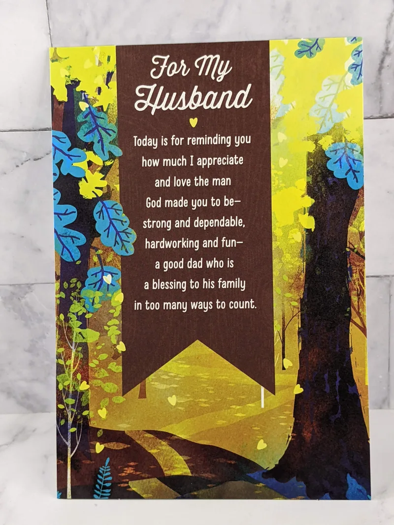 A religious Father's Day greeting card for a husband, with a yellow and blue forest image on the front cover.