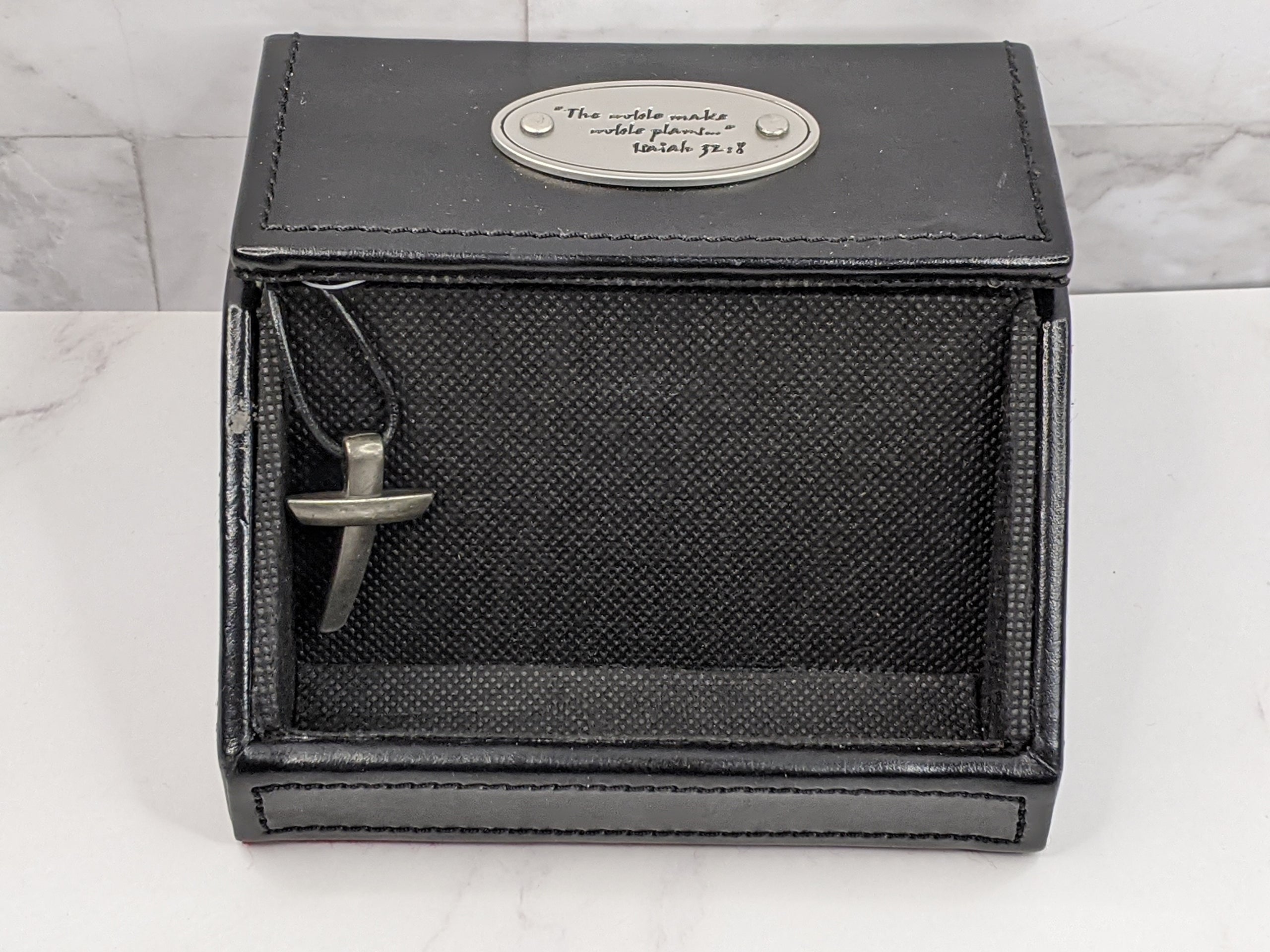 A black business card holder for a pastor with a Bible verse inscribed on a metal plate and a silver cross charm. 