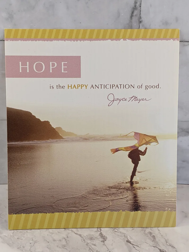 A Christian hope and friendship greeting card with an image of a person ready to release a kite as they are standing on a beach with water.