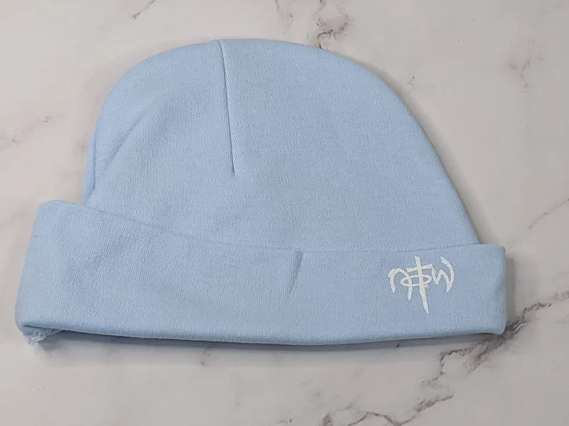 A knit light blue baby hat with a NOTW logo.