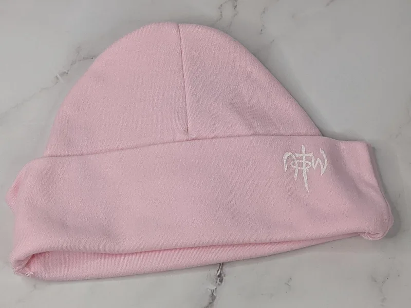 A knit light pink baby hat with a NOTW logo.
