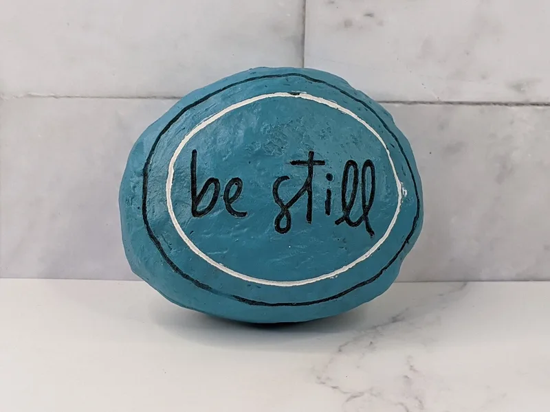 An aqua blue resin rock that is embossed with the words "be still."